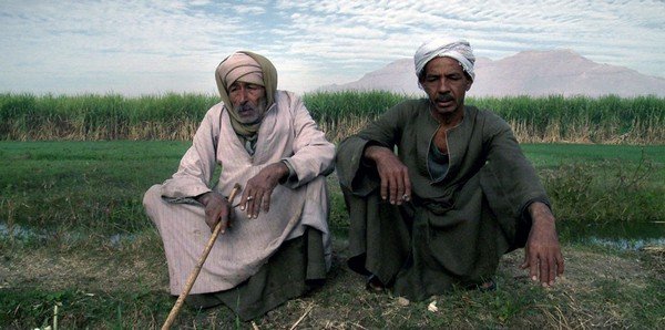 Photographie de deux hommes assis assis et enturbannés au bord d'une route
