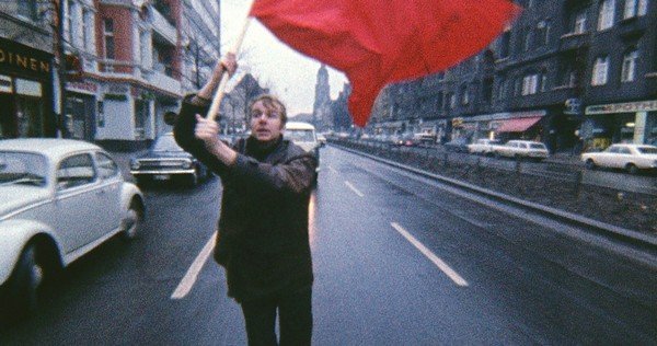 Photographie d'un jeune homme brandissant un drapeau rouge dans ka rue