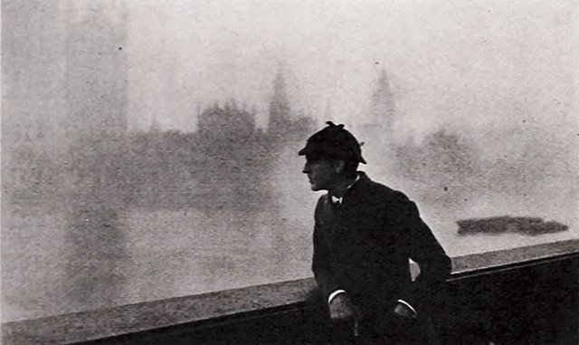 Photo en noir et blanc montrant un homme vétu comme Sherlock Holmes, accoudé à une balustrade au bord de la Tamise.